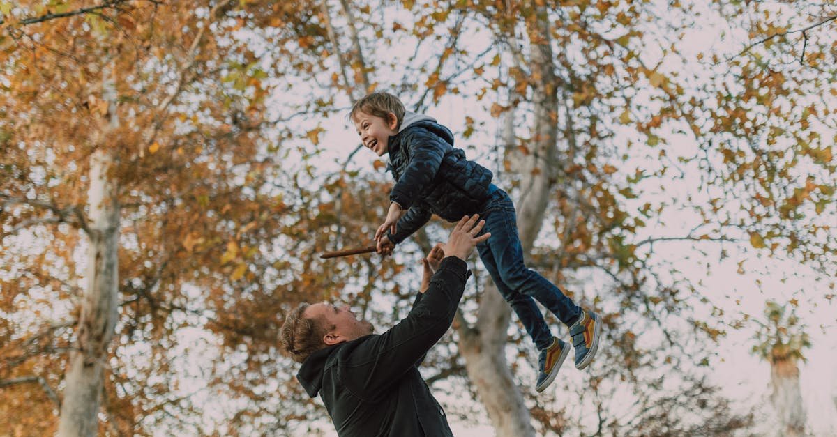 Joyful father and son bonding by playing in a fall park under colorful leaves.